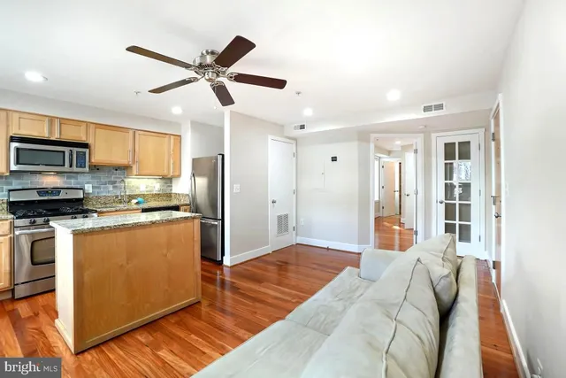 a open kitchen with stainless steel appliances granite countertop a refrigerator oven a sink dishwasher and white cabinets with wooden floor