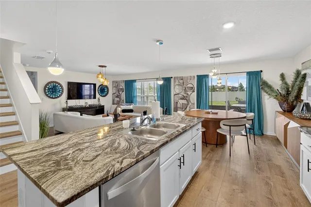 a kitchen with kitchen island granite countertop a stove top oven a sink a dining table and chairs with wooden floor