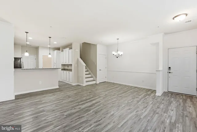 an empty room with wooden floor and kitchen view