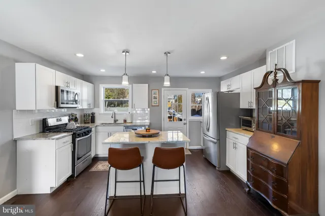 a kitchen with stainless steel appliances kitchen island granite countertop a stove a refrigerator a sink dishwasher a dining table and chairs with wooden floor