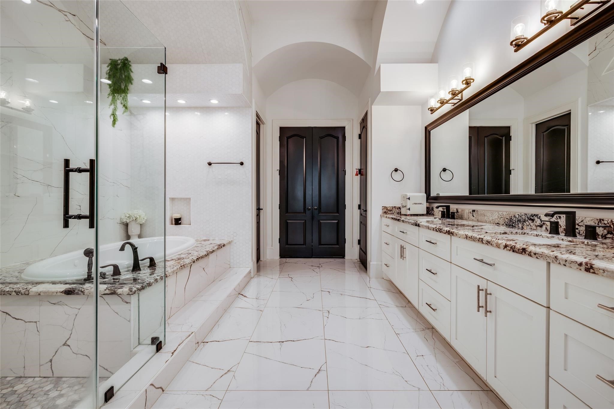 4821 Walters Road Richmond, TX 77469 - Photo 33 of 50 This spa-inspired luxury bathroom showcases sleek contemporary design with floor-to-ceiling marble-style finishes, elegant black fixtures, and a seamless glass-enclosed walk-in shower. The oversized soaking tub is beautifully framed by dramatic stone detailing and recessed lighting, creating a relaxing retreat with a high-end hotel feel. Clean architectural lines, custom niche shelving, and sophisticated textures throughout the space blend modern elegance with everyday comfort.