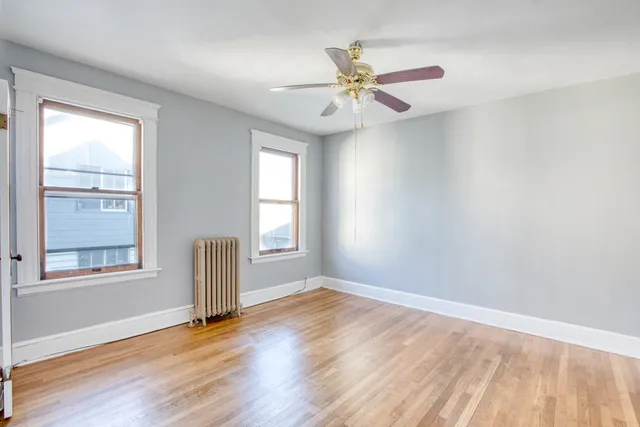 an empty room with wooden floor fan and windows