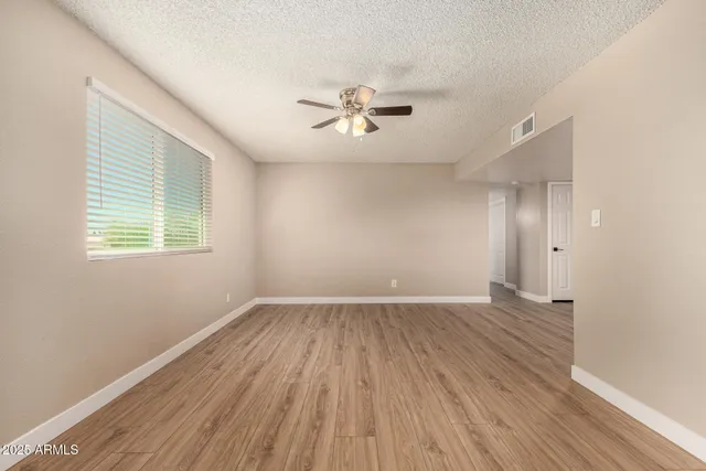 an empty room with wooden floor ceiling fan and windows