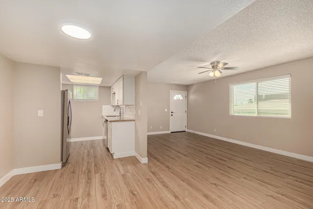 an empty room with wooden floor kitchen view and windows