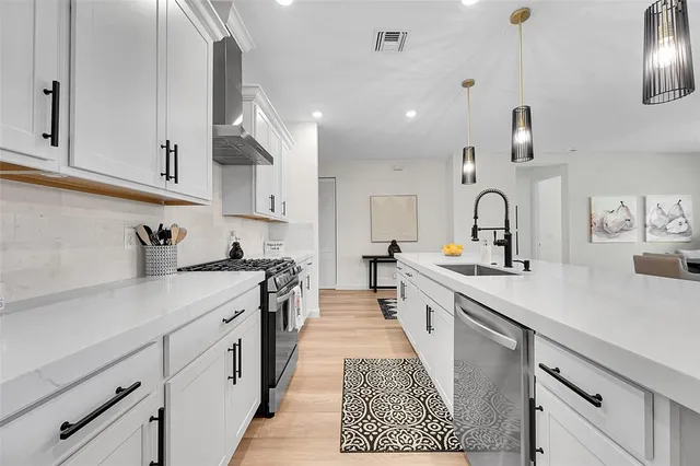 a large kitchen with stainless steel appliances granite countertop a sink dishwasher a stove and white cabinets with wooden floor