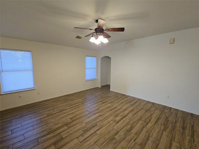 a view of an empty room with wooden floor and a ceiling fan