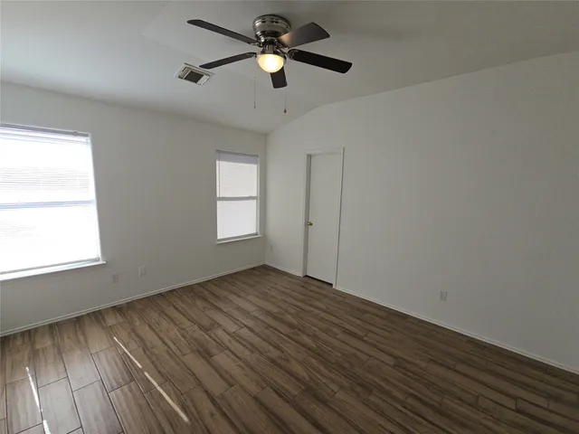 an empty room with wooden floor ceiling fan and windows
