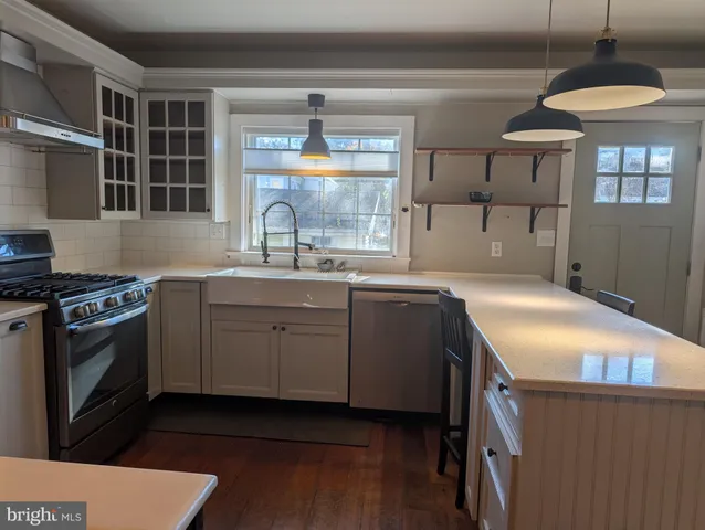 a kitchen with stainless steel appliances kitchen island granite countertop a refrigerator a sink dishwasher and white cabinets with wooden floor