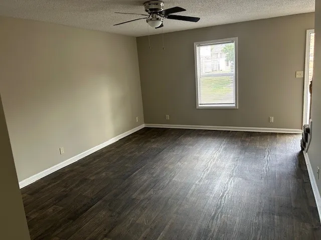 an empty room with wooden floor chandelier fan and windows