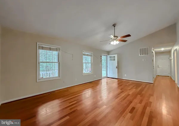 a view of an empty room with wooden floor and a ceiling fan