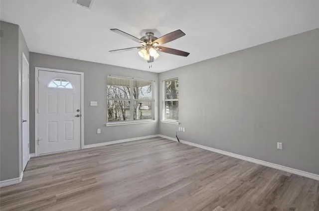 a view of an empty room with chandelier fan and wooden floor