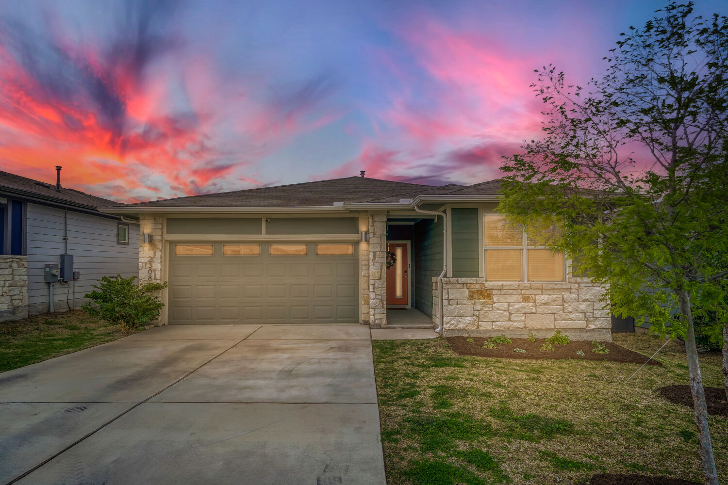 2308 Ranier Court Austin, TX 78754 - Photo 27 of 29 Ranch-style home featuring an attached garage, stone siding, driveway, and a front lawn beautiful sunset.
