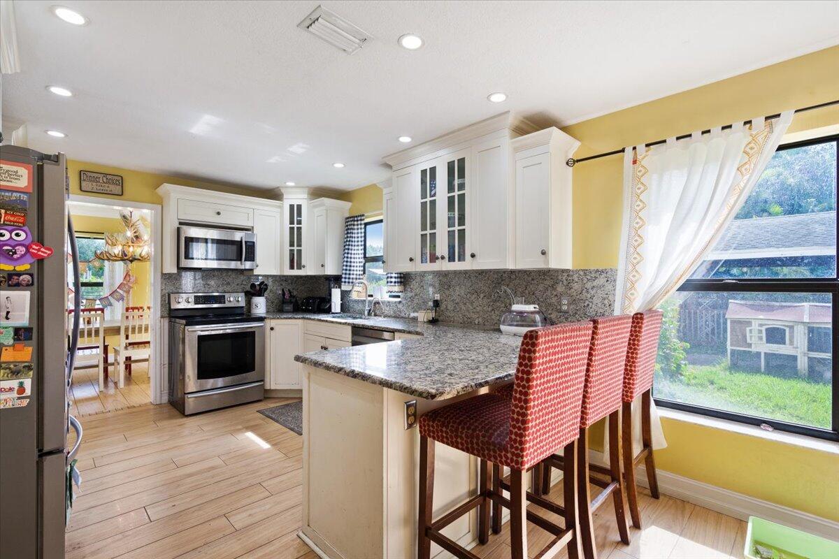 1350 C Road Loxahatchee Groves, FL 33470 - Photo 2 of 27 a kitchen with stainless steel appliances granite countertop a stove top oven a sink dishwasher and a refrigerator with wooden floor