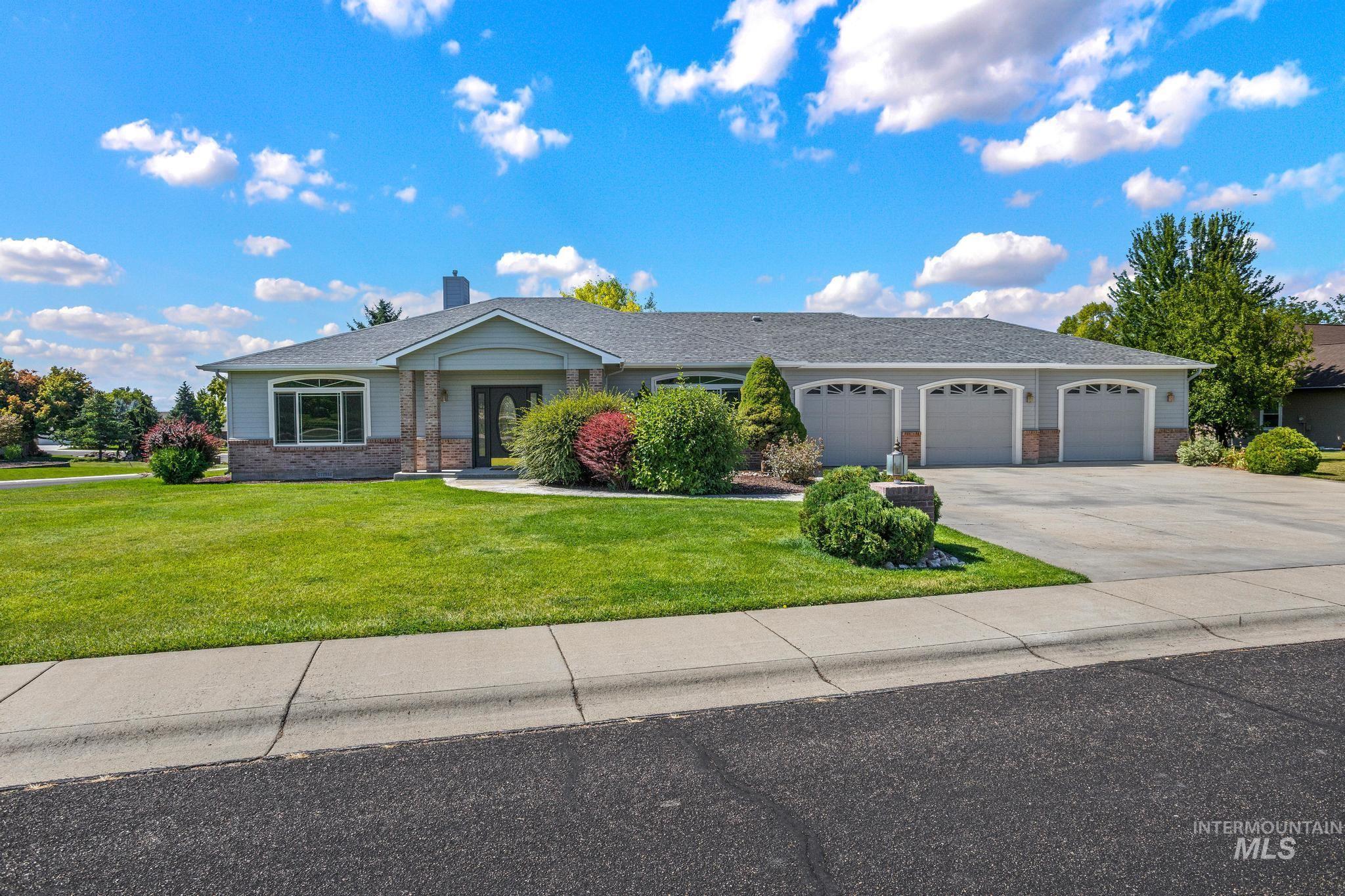 15181 Drury Way Caldwell, ID 83607 - Photo 34 of 49 Ranch-style exterior featuring a three-car garage, manicured lawn, stone accents, and mature landscaping