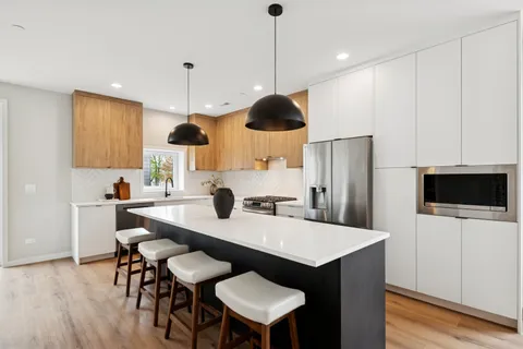 a kitchen with stainless steel appliances a stove a refrigerator a microwave a dining table and chairs with wooden floor