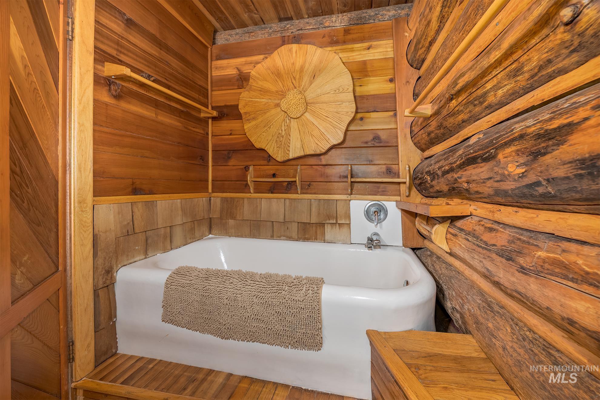 2150 Seid Creek Road Cambridge, ID 83610 - Photo 18 of 50 Bathtub with wood-paneled walls and log construction, featuring a chrome faucet and a wood-slatted floor