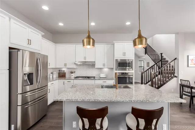 a kitchen with stainless steel appliances kitchen island granite countertop a refrigerator a stove a sink a dining table and chairs with wooden floor