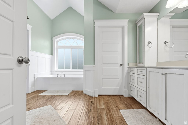 672 Perry Hollow Drive Mapleton, UT 84664 - Photo 48 of 106 Bathroom featuring wood-finish flooring, a built-in soaking tub with arched window, vaulted ceiling, and white vanity with storage cabinetry and drawers