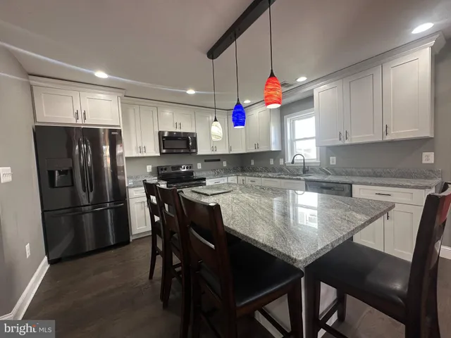 a kitchen with granite countertop a refrigerator a stove a kitchen island with a dining table and chairs