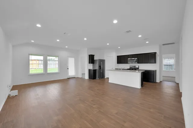 a view of kitchen with kitchen island granite countertop a stove top oven and a sink with wooden floor