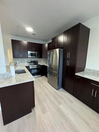 a kitchen with stainless steel appliances kitchen island granite countertop wood cabinets a refrigerator and a sink