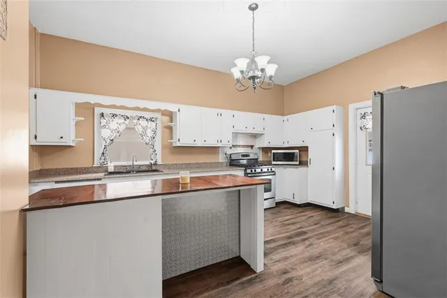 a kitchen with stainless steel appliances granite countertop a refrigerator a sink dishwasher a stove and white countertops with wooden floor