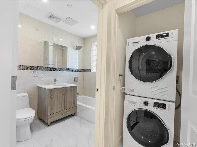 124-28 Queens Boulevard, Unit 9D Queens, NY 11415 - Photo 12 of 14 Full bathroom featuring stacked washing machine and dryer, tile walls, vanity, and light marble finish flooring