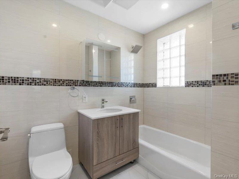 124-28 Queens Boulevard, Unit 9D Queens, NY 11415 - Photo 13 of 14 Bathroom featuring tile walls, vanity, and bathtub / shower combination
