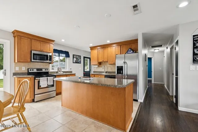 a kitchen with stainless steel appliances granite countertop a refrigerator a stove top oven a sink dishwasher and white cabinets with wooden floor