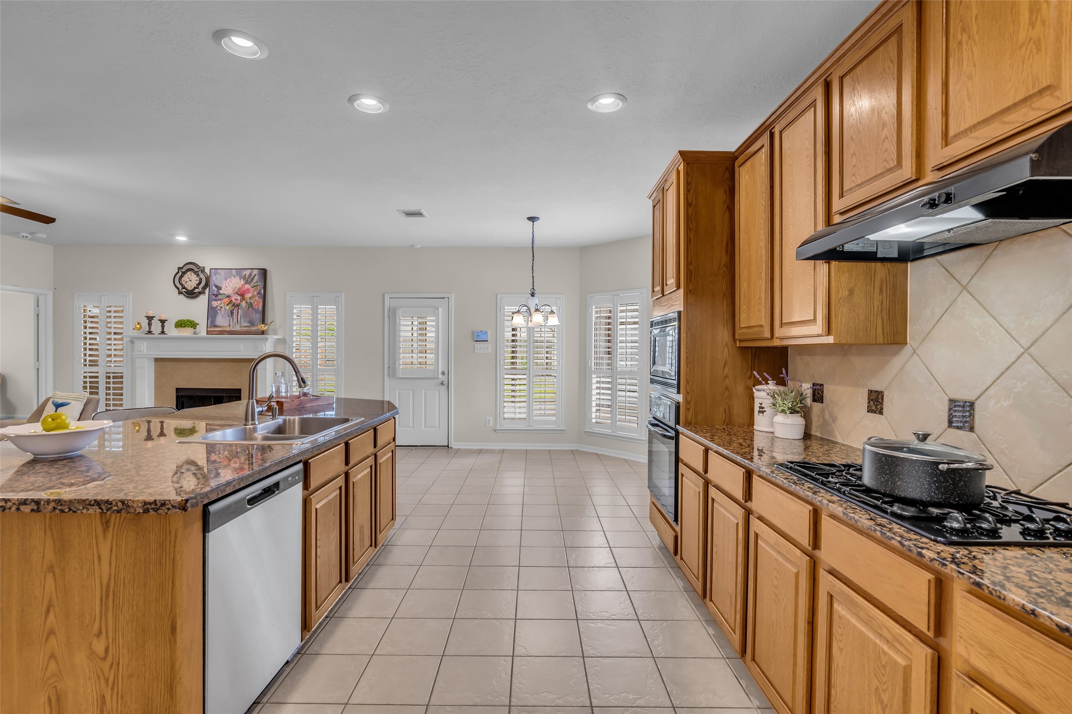 6807 Chapelfield Lane Houston, TX 77049 - Photo 13 of 42 This spacious kitchen features granite countertops, ample wooden cabinetry, and modern appliances. It opens into a bright living area with a cozy fireplace and large windows, creating a welcoming atmosphere.