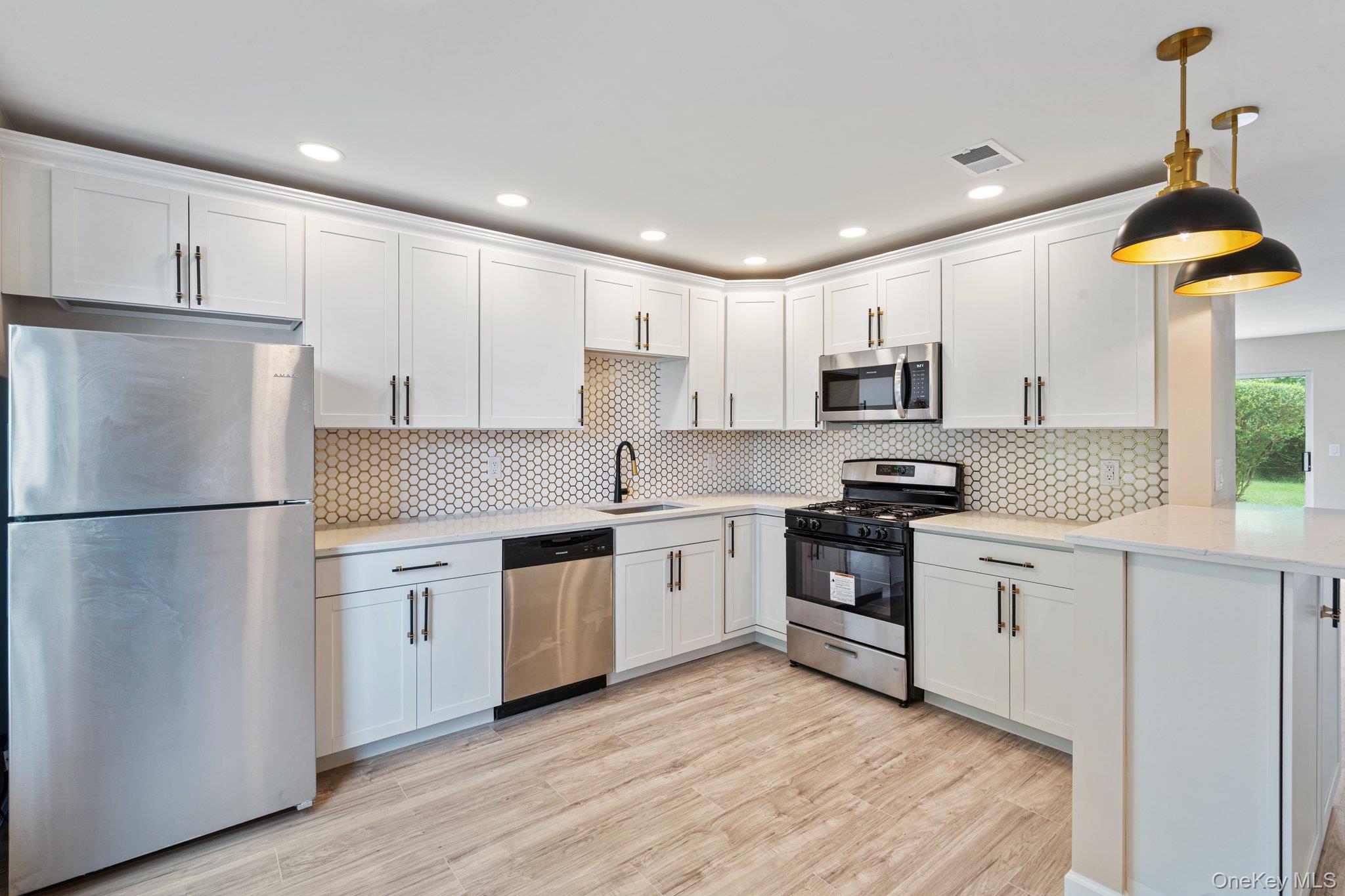 6 Doe Path Coram, NY 11727 - Photo 4 of 48 Kitchen featuring appliances with stainless steel finishes, white cabinetry, light countertops, light wood-style floors, and backsplash