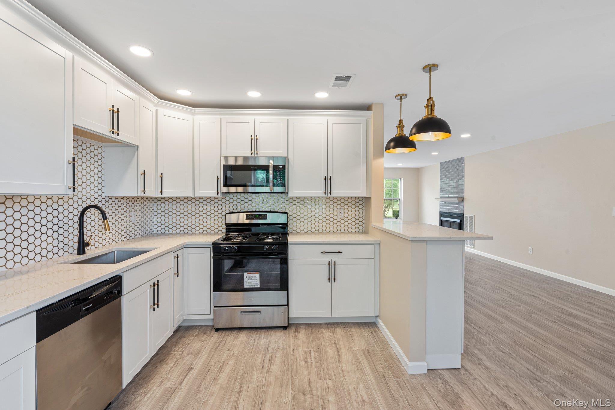 6 Doe Path Coram, NY 11727 - Photo 6 of 48 Kitchen featuring appliances with stainless steel finishes, a peninsula, light wood finished floors, white cabinets, and tasteful backsplash