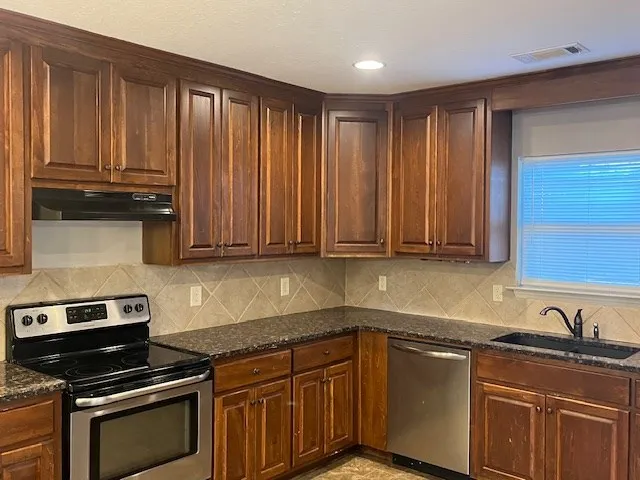 a kitchen with granite countertop a stove a sink dishwasher and cabinets