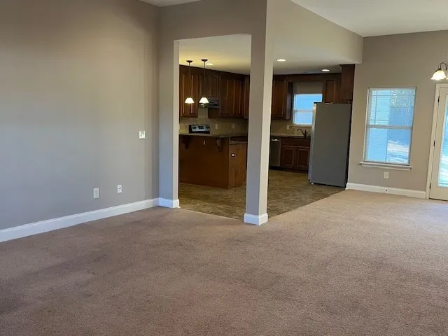 a view of an empty room with kitchen and a window