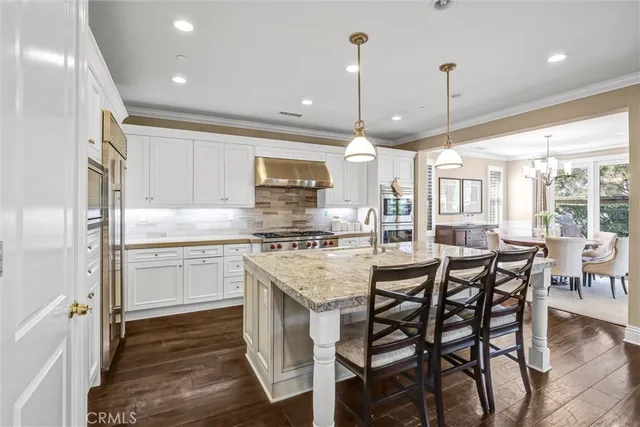 a kitchen with stainless steel appliances granite countertop a stove top oven a refrigerator a sink and chairs