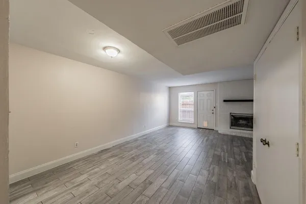 an empty room with wooden floor fireplace and windows