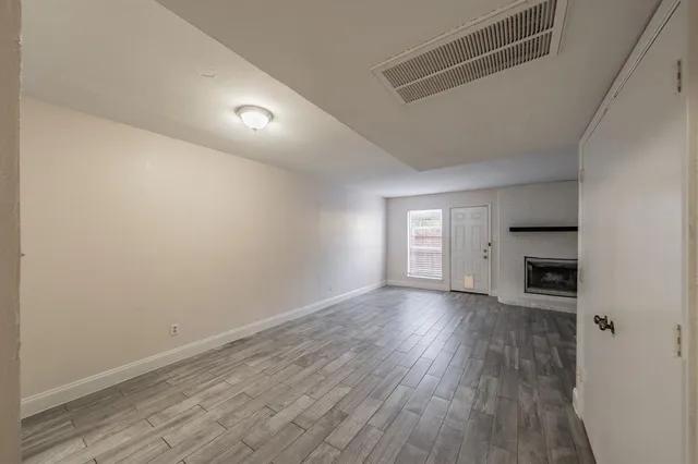 an empty room with wooden floor fireplace and windows