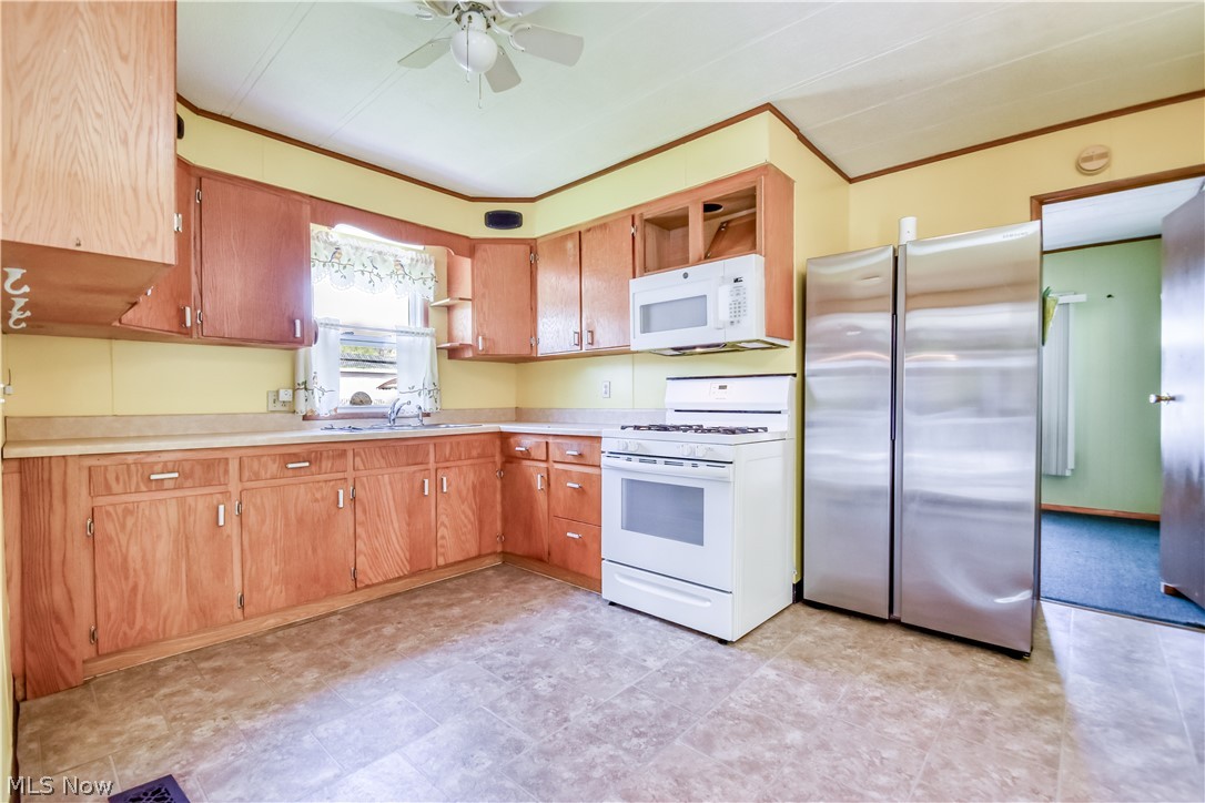 112 Lakeside Way Southwest Warren, OH 44481 - Photo 6 of 16 Kitchen featuring wood cabinetry, white appliances including a range and microwave, stainless steel refrigerators, and patterned vinyl flooring