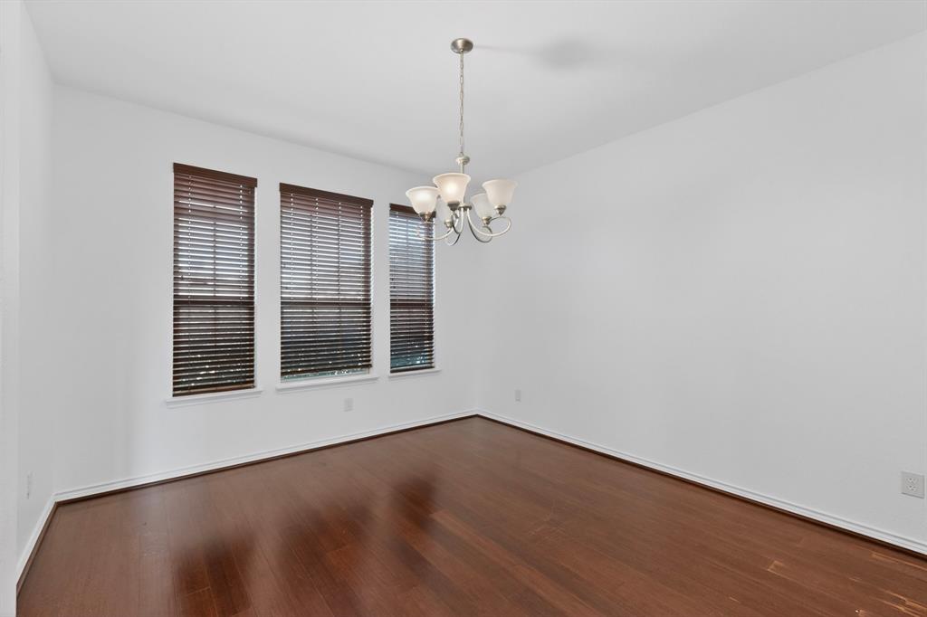 426 Harding Lane Lavon, TX 75166 - Photo 5 of 40 Spacious room featuring rich wood-finish flooring, three large windows with dark wood blinds, white baseboards, and a classic chandelier with frosted glass shades