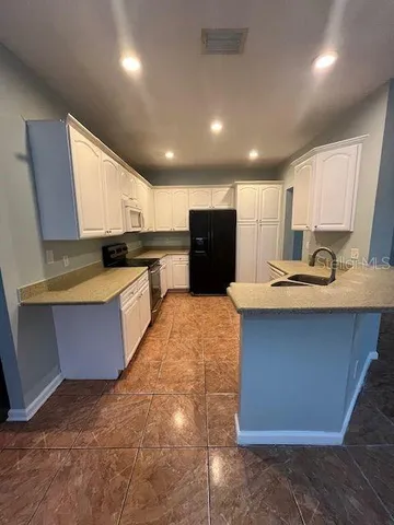 a kitchen with kitchen island granite countertop a stove a sink a refrigerator and white cabinets with wooden floor