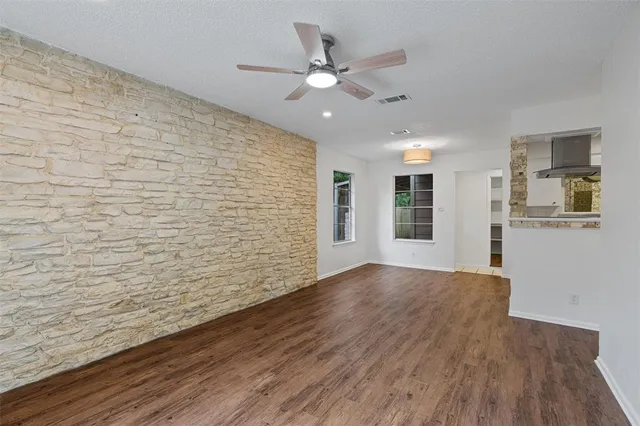 a view of an empty room with wooden floor and a ceiling fan