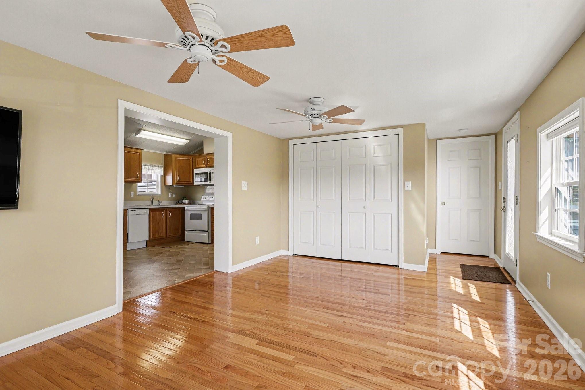 122 Maple Street New London, NC 28127 - Photo 5 of 29 a view of a livingroom with a kitchen space with wooden floor a ceiling fan and windows