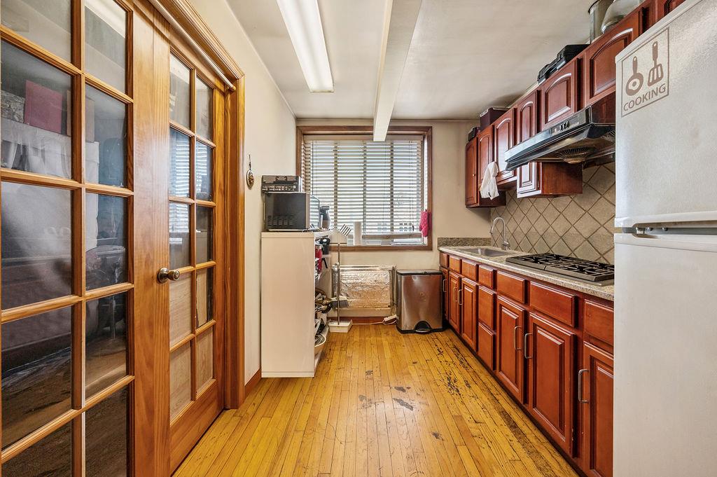 43-07 162nd Street Queens, NY 11358 - Photo 10 of 18 Kitchen with under cabinet range hood, freestanding refrigerator, light wood-style floors, stainless steel gas cooktop, and decorative backsplash