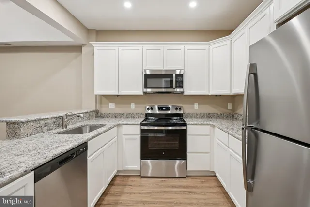 a kitchen with stainless steel appliances granite countertop a stove top oven a sink dishwasher and a refrigerator with wooden floor