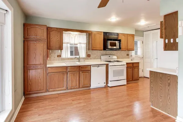 a kitchen with stainless steel appliances granite countertop a stove top oven a sink a refrigerator with white cabinets and wooden floor