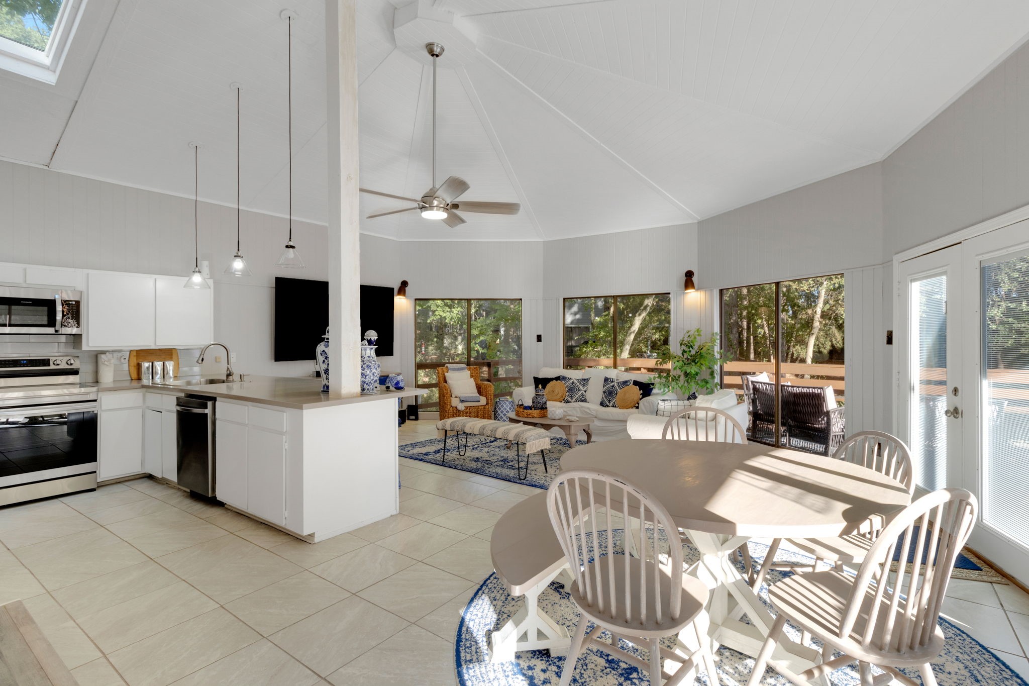 Open-concept kitchen, dining, and living area with large windows providing natural light and views of the surrounding trees.