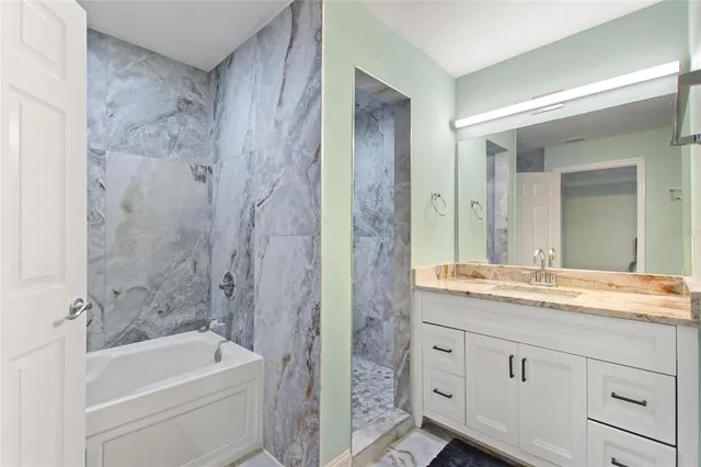 a bathroom with a granite countertop sink a mirror a bathtub and shower