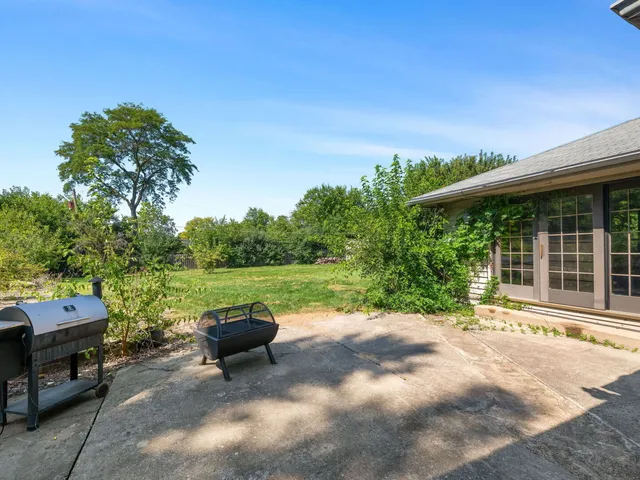 a view of a patio with table and chairs under an umbrella with large trees