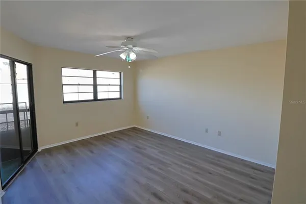an empty room with wooden floor chandelier fan and windows