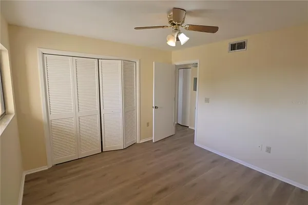 an empty room with wooden floor fan and windows